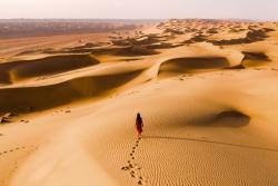 Wahiba Sands - pieskové duny a kráčajúca žena. Omán. Foto: adobe.com