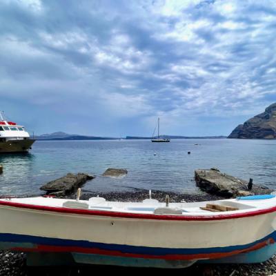 Prístav ostrova Thirasia, malá loď a pláž, v pozadí sopečné ostrovy. Santorini.