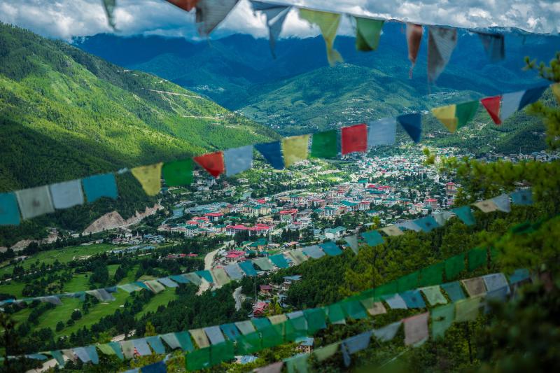 Pohľad z výšky na farebné domy a zelené kopce mesta Thimphu v Butáne.