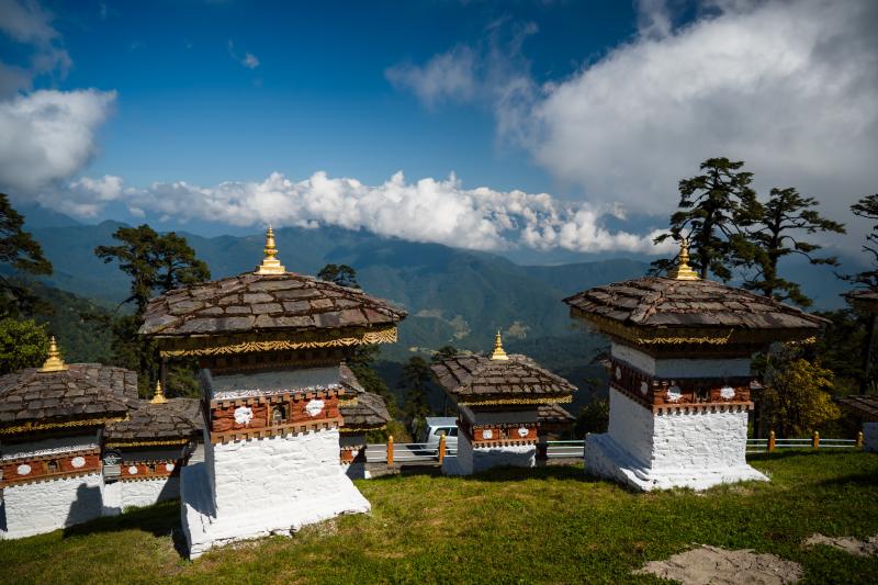 Biele pamätníky so strieškou a výhľadom na butánsky priesmyk Dochula. 