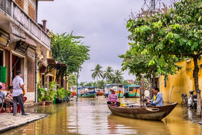 Farebné domy, chodec a ženy plaviace sa na drevenej ľodke v Hoi An vo Vietname.