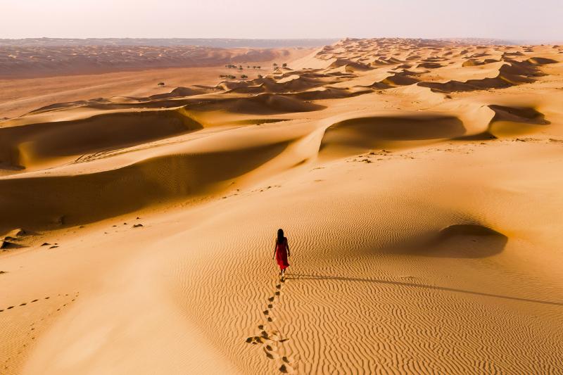 Wahiba Sands - pieskové duny a kráčajúca žena. Omán. Foto: adobe.com