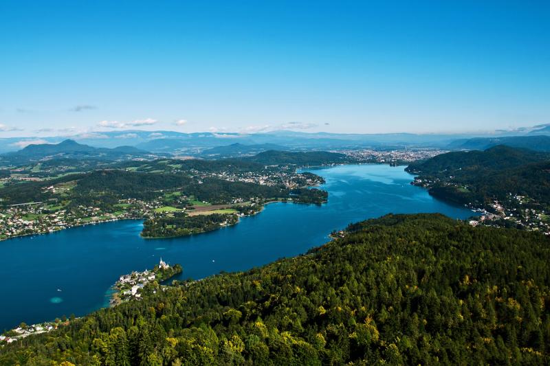 Moderné jazero Wörthersee, zelené stromy, pohorie a mestá pri jazere. Rakúsko