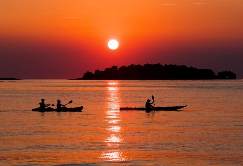 Zapadajúce slnko, ostrovy a ľudia na kajakoch. Rovinj.