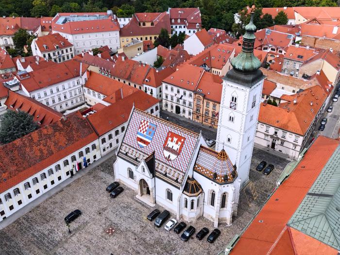 Historické budovy s červenými strechami a kostol v centre Záhrebu.