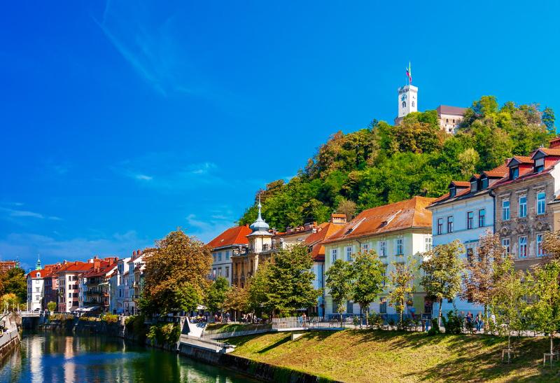 Historické budvy popri rieke a hrad týčiaci sa na kopci s vlajkou.