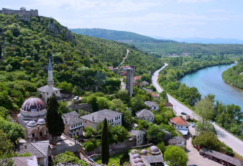 Mešita s minaretom, hrad na kopci a domy pri rieke.